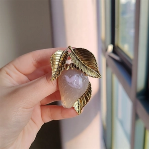 Close-up of translucent strawberry brooch with golden metal leaves held in hand