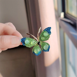 Modieuze vlinderbroche met groene en blauwe kristallen op een gouden metalen voet