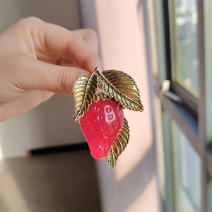 Detailed close-up showing glossy red resin strawberry brooch with golden leaves texture