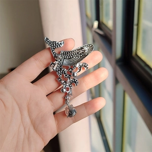 Detail of vintage whale brooch with textured silver finish and droplet pendant