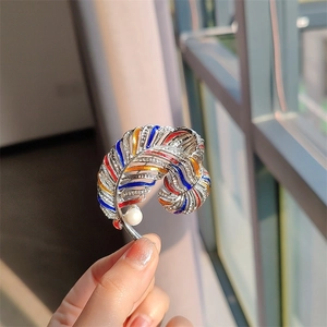Detailed close-up of a colorful enamel feather brooch with crystals and a white pearl