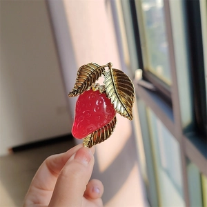 Close-up of a jelly resin strawberry brooch with gold metal leaves held in hand