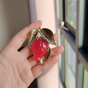 Detailed view of 3D resin strawberry brooch with golden metallic leaves held in hand