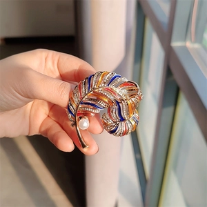 Detail of vintage gold feather brooch with colorful enamel, rhinestones and faux pearl