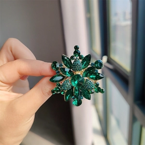 Detalle de broche de flor vintage con cristales verdes y aleación dorada sostenido a mano