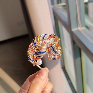 Macro view of gold feather brooch with colorful enamel, crystal accents and white pearl