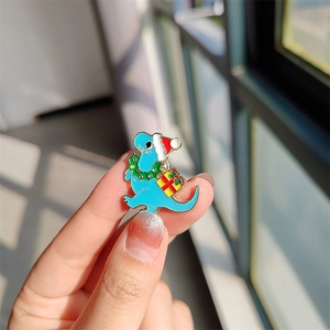 Détail d'un pin's dinosaure de Noël bleu avec bonnet de fête et boîte cadeau en émail