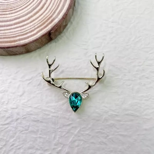 Élégante broche renne dorée avec un grand cristal émeraude en goutte sur fond blanc