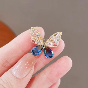 Spilla a farfalla dorata con cristalli blu sfumati e intarsio di zirconi sulla mano