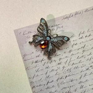 Vintage butterfly brooch with amber red crystal and rhinestones on retro paper