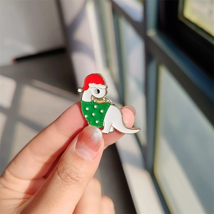 Détail du pin's dinosaure de Noël en émail blanc portant un bonnet rouge et un pull vert