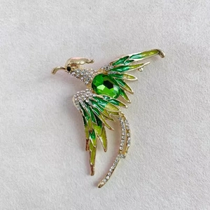 Détail macro d'une broche phénix de luxe avec cristaux verts et ailes émaillées dorées