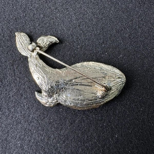 Detailed back view of golden whale brooch showing safety pin and textured metal finish