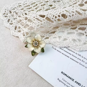 Broche fleur de gardénia avec pétales crème, perles dorées et feuilles en émail vert