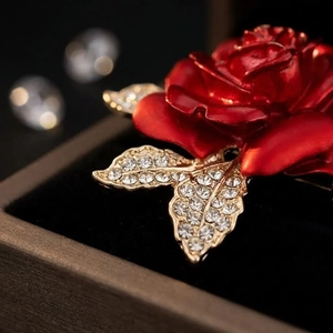 Exquise broche rose rouge avec feuilles de cristal dorées sur une boîte à bijoux