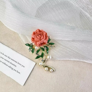 Dettaglio macro della spilla fiore rosa rossa con foglie di smalto verde e perle bianche