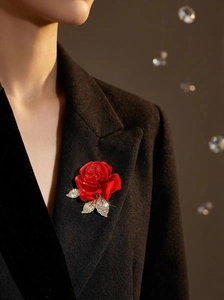 Détail d'une broche rose rouge avec feuilles diamantées épinglée sur un revers noir