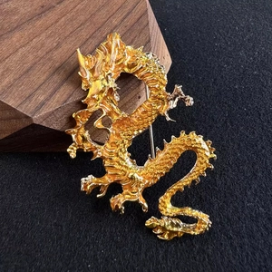 Goldene Drachen-Brosche mit feiner Schuppentextur auf elegantem grauem Stoffhintergrund