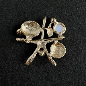 Vue macro du dos de la broche coquillage dorée avec une perle et fermoir épingle