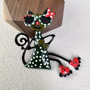 Cute spotted cat brooch with sunglasses and red bow tie on a textured stone background