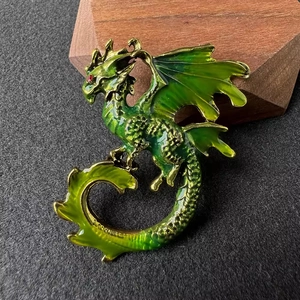Macro d'une broche dragon en émail vert avec œil en pierre rouge sur support bois
