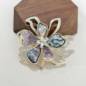 Elegant floral brooch with iridescent faux shell petals and purple crystals on wood stand