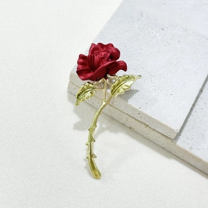 Exquisite red rose brooch with matte petals and golden stem on white travertine background