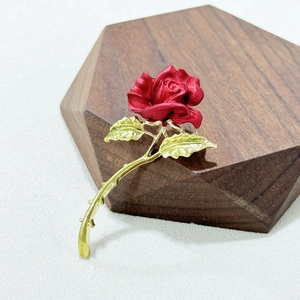Exquisite red rose brooch with green leaves and gold stem on dark wood pedestal