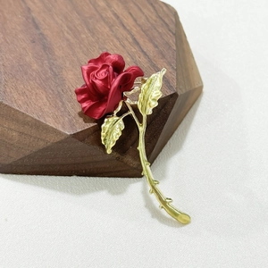 Romantic red rose brooch with matte petals and golden metallic stem on a dark wooden base