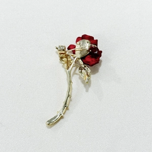 Detail of red rose brooch with golden stem and layered petals on white fabric