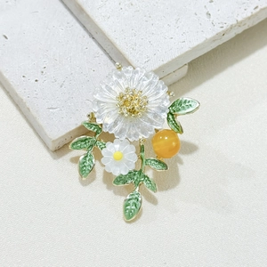 Elegant white daisy floral brooch with green leaves and golden stamen on stone surface