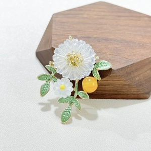 Elegant daisy brooch with pink frosted petals and green enamel leaves on a wooden stand