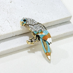 Elegant gold parrot brooch with sparkling crystals and colorful enamel on stone texture