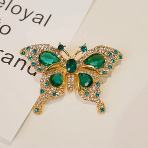 Luxury gold butterfly brooch with green gems and blue crystals on a beige background