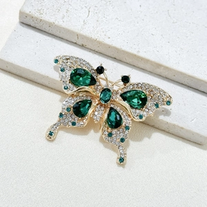 Detailed close-up of butterfly brooch with emerald green gems and sparkling crystals