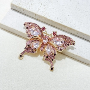 Elegant gold butterfly brooch with pink gemstones and purple crystals on white stone