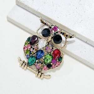 Macro detail of owl brooch with colorful faceted gemstones on golden metallic branch