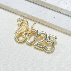 2025 Snake Year brooch in golden metal with rhinestones on white fabric background