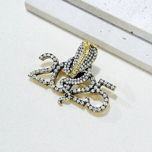 Golden 2025 snake brooch with sparkling crystals and serpent figure on white background