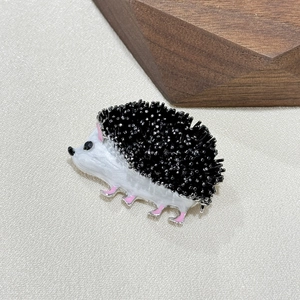 Cartoon hedgehog brooch with black spines and white enamel on textured background