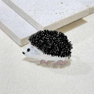 Adorable white enamel hedgehog brooch with black quills and silver beads on a stone background