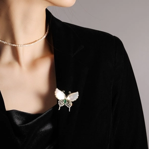 Macro detail of natural shell butterfly brooch with emerald green stone on black velvet lapel