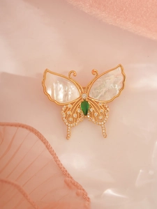Detail of golden butterfly brooch with iridescent natural shell wings and green gemstone