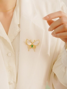 Exquisite butterfly brooch with white shell wings and emerald green gemstone on white blazer