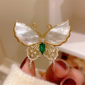 Macro detail of butterfly brooch with white shell wings and green emerald gemstone