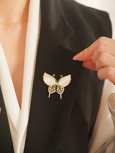 Close-up of a luxury butterfly brooch with shell wings and green gemstone on clothing