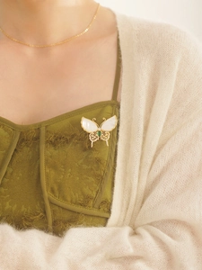 Macro detail of butterfly brooch featuring natural shell wings and emerald green gemstone