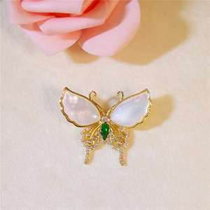 Exquisite butterfly brooch with shell wings and emerald accent on a beige texture