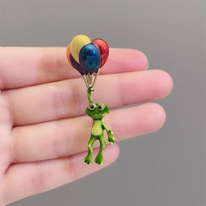 Détail d'une broche en émail avec grenouille et ballons colorés, finition brillante