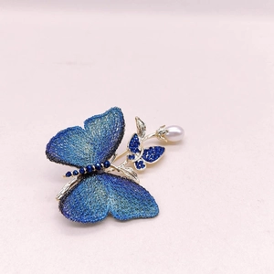 Détail de la broche papillon bleue avec texture brodée et perle sur support doré